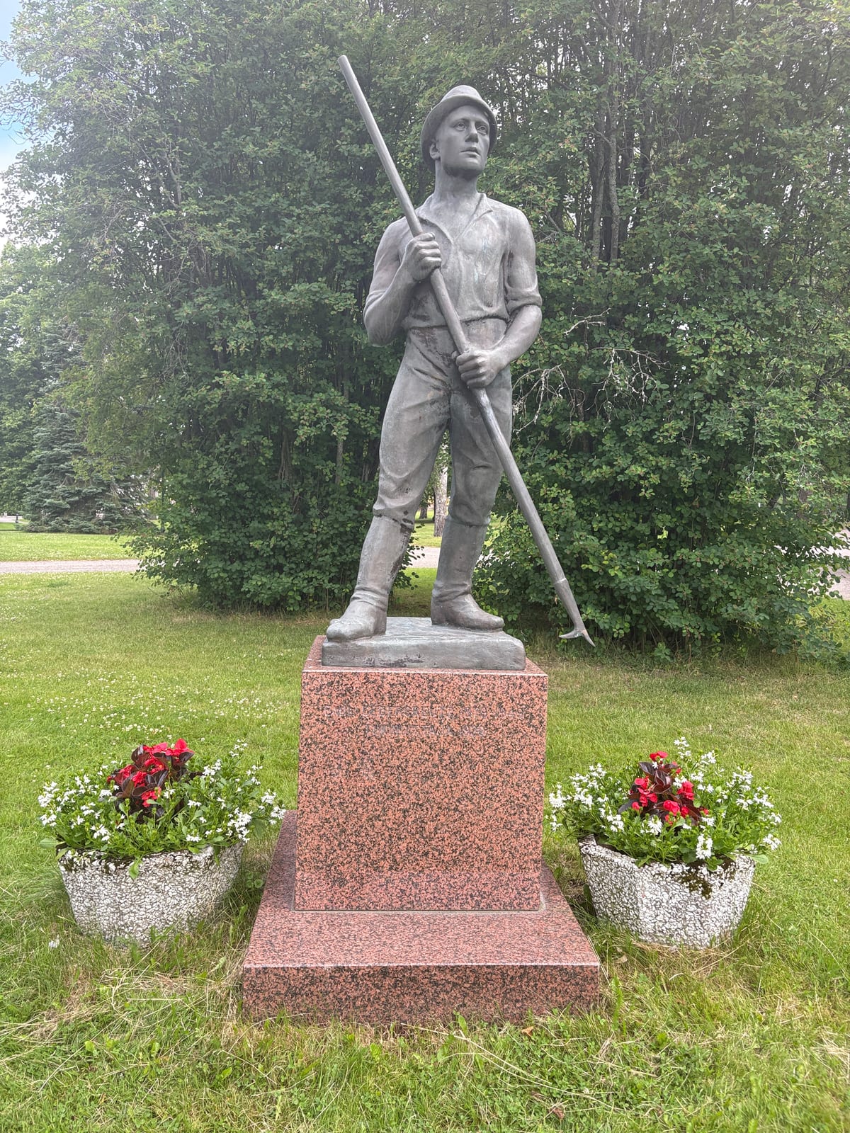 Uittomiehen patsas graniittijalustalla, keksi kädessä ja kukkien ympäröimänä